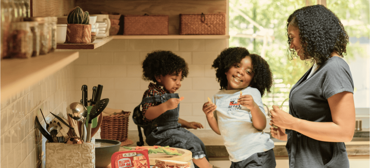 Mother happily staring at her two kids while they have snacks in the kitchen